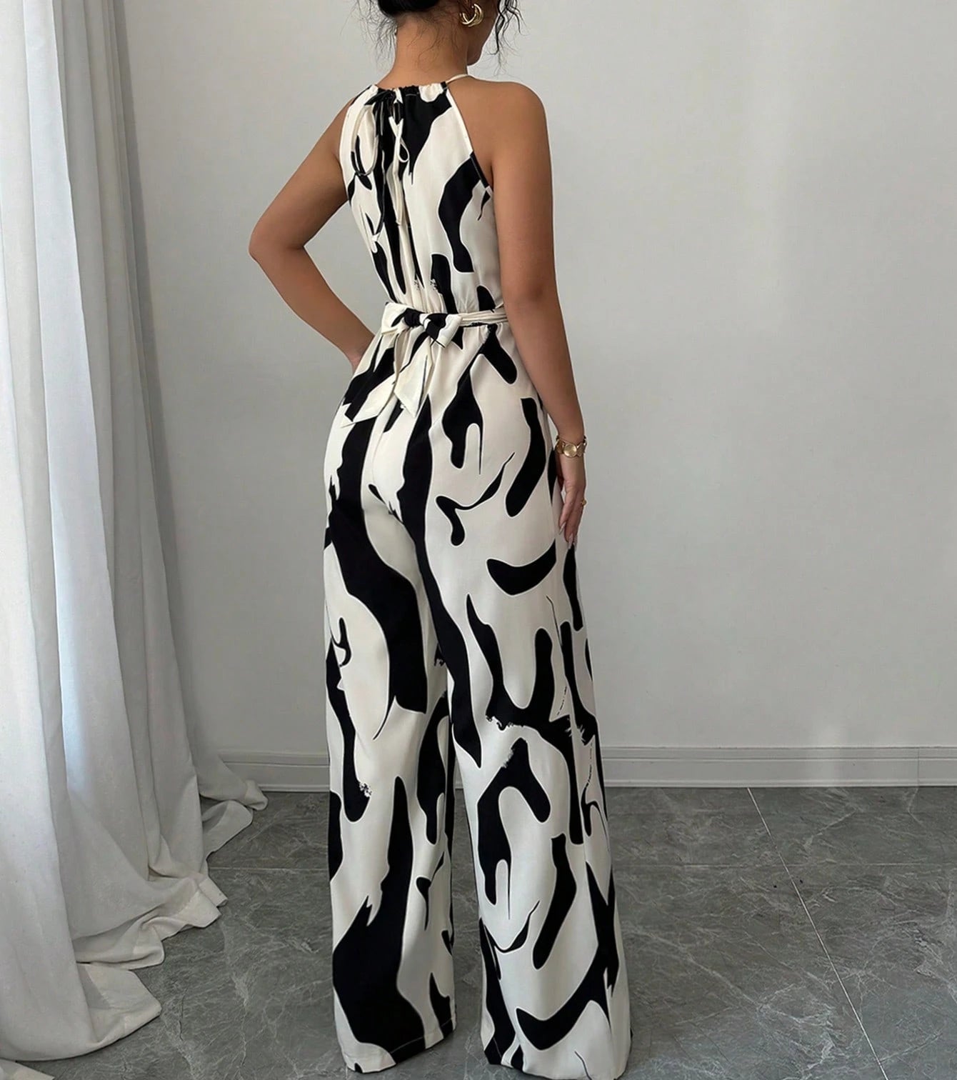 Person wearing a black and white patterned jumpsuit in a room with white curtains and gray floor.