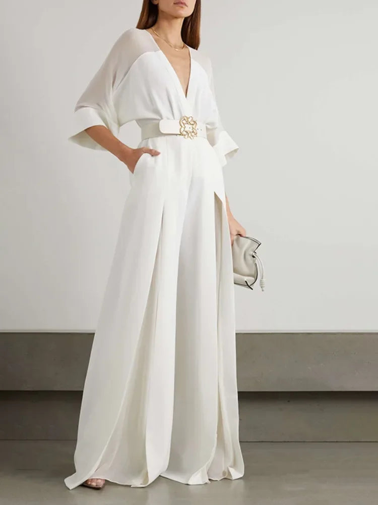 Woman wearing a white dress with a belt and clutch against a plain background