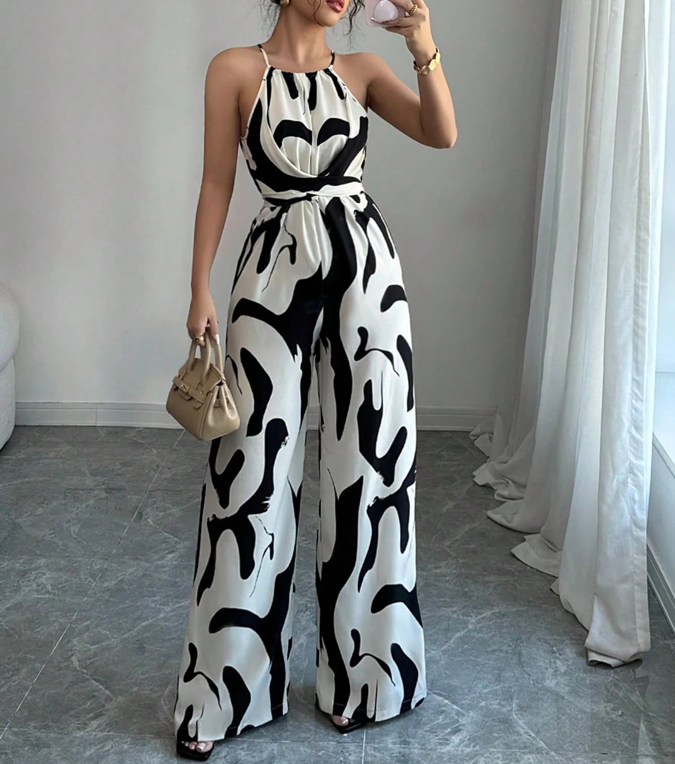 Woman wearing a black and white patterned jumpsuit in a room with a gray floor and white curtains.