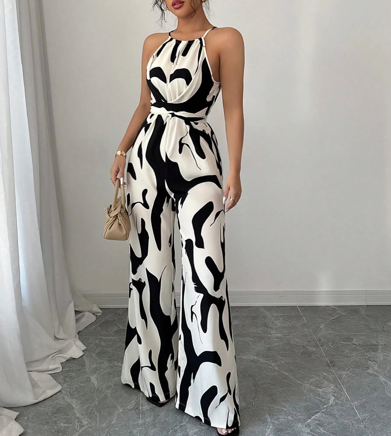 Woman wearing a black and white patterned jumpsuit in a room with white curtains and gray floor.