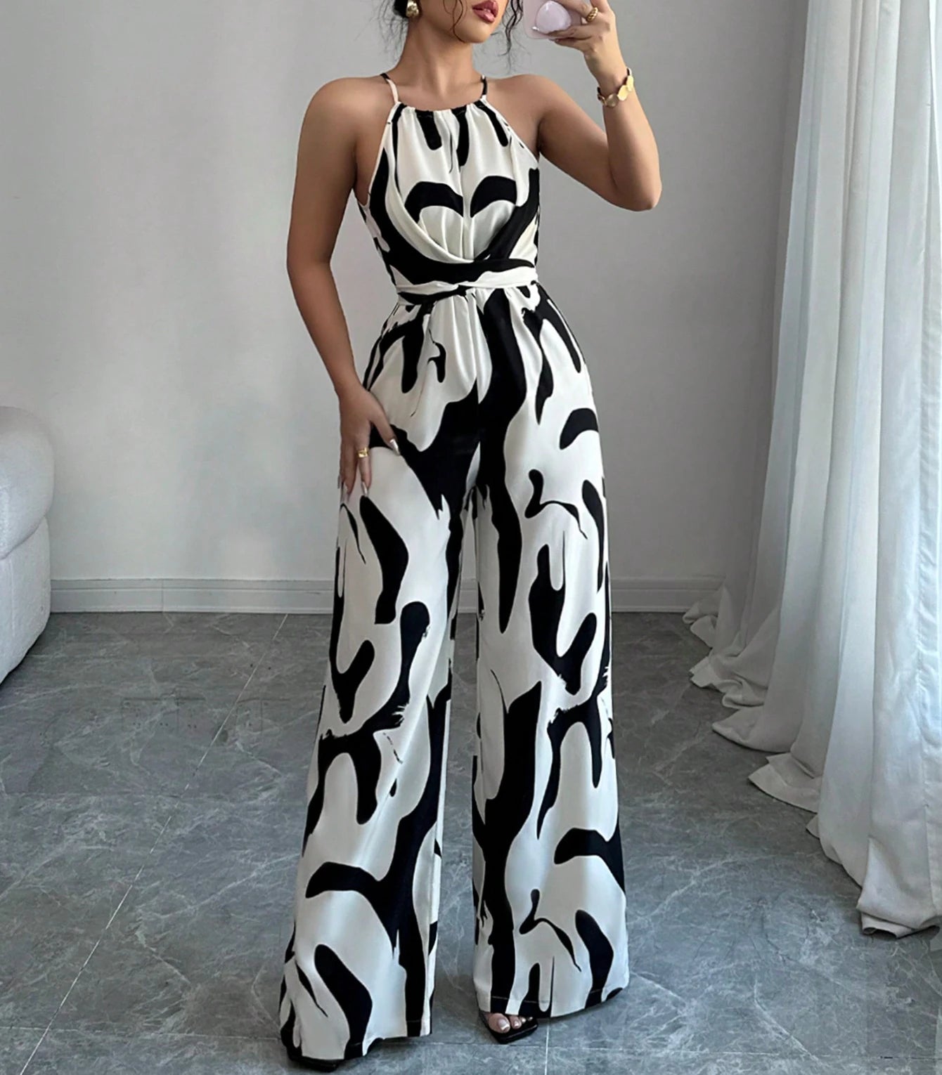 Woman wearing a black and white patterned jumpsuit in a room with a gray floor and white curtains.
