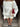 A person wearing an off-shoulder white solid knit sweater paired with a skirt, accessorized with a beige handbag, red brooch, and black shoes.