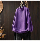 A red vintage turtleneck pullover sweater hanging against a wooden background.