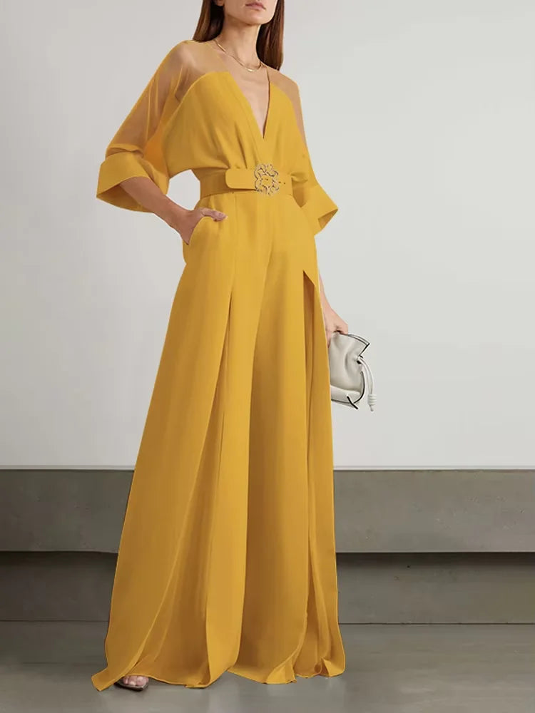 Woman wearing a yellow evening gown with a deep neckline and long sleeves on a plain background