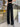 A pair of black wide-leg suit pants with a high waist fit and straight legs, worn by a person standing in a casual setting.